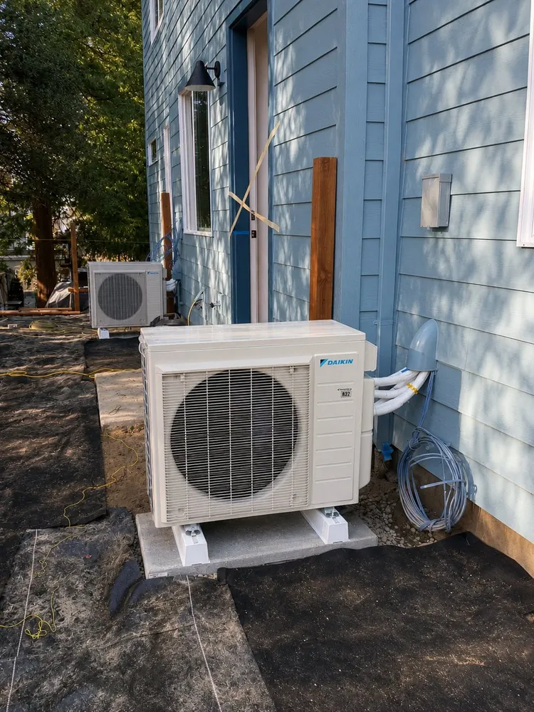 White ductless outdoor unit on a pad beside blue siding