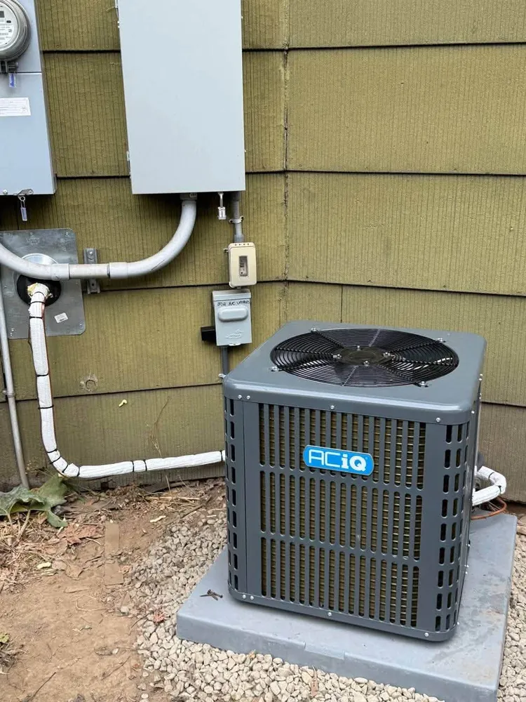 Outdoor condenser on a concrete pad beside electrical meters on an olive wall