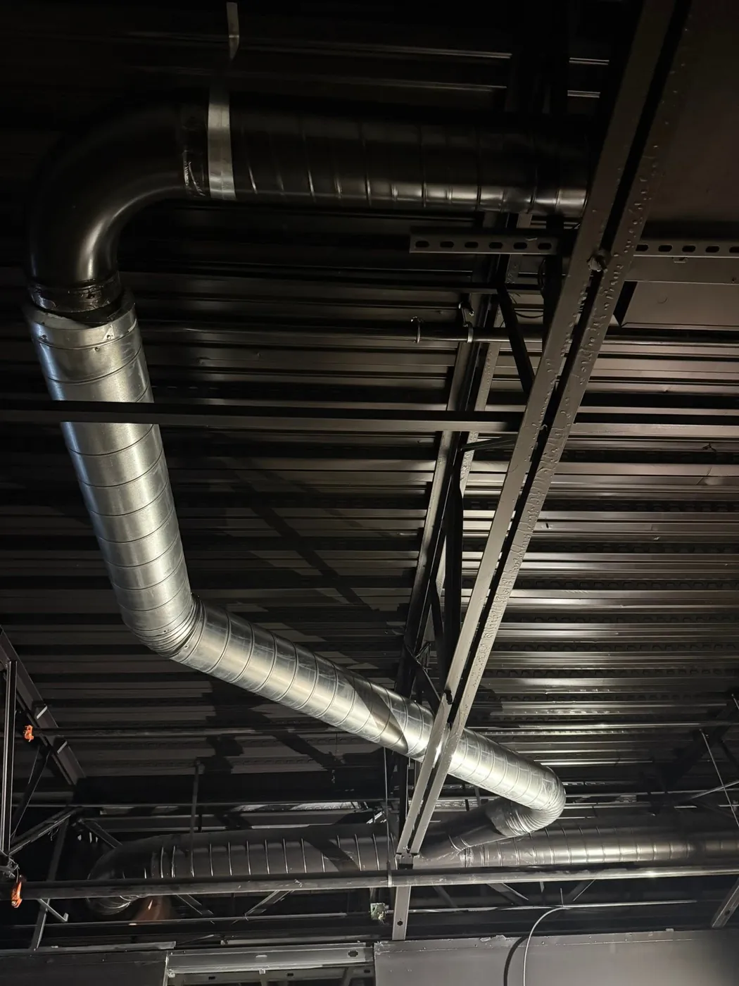 Round metal duct running along dark ceiling beams