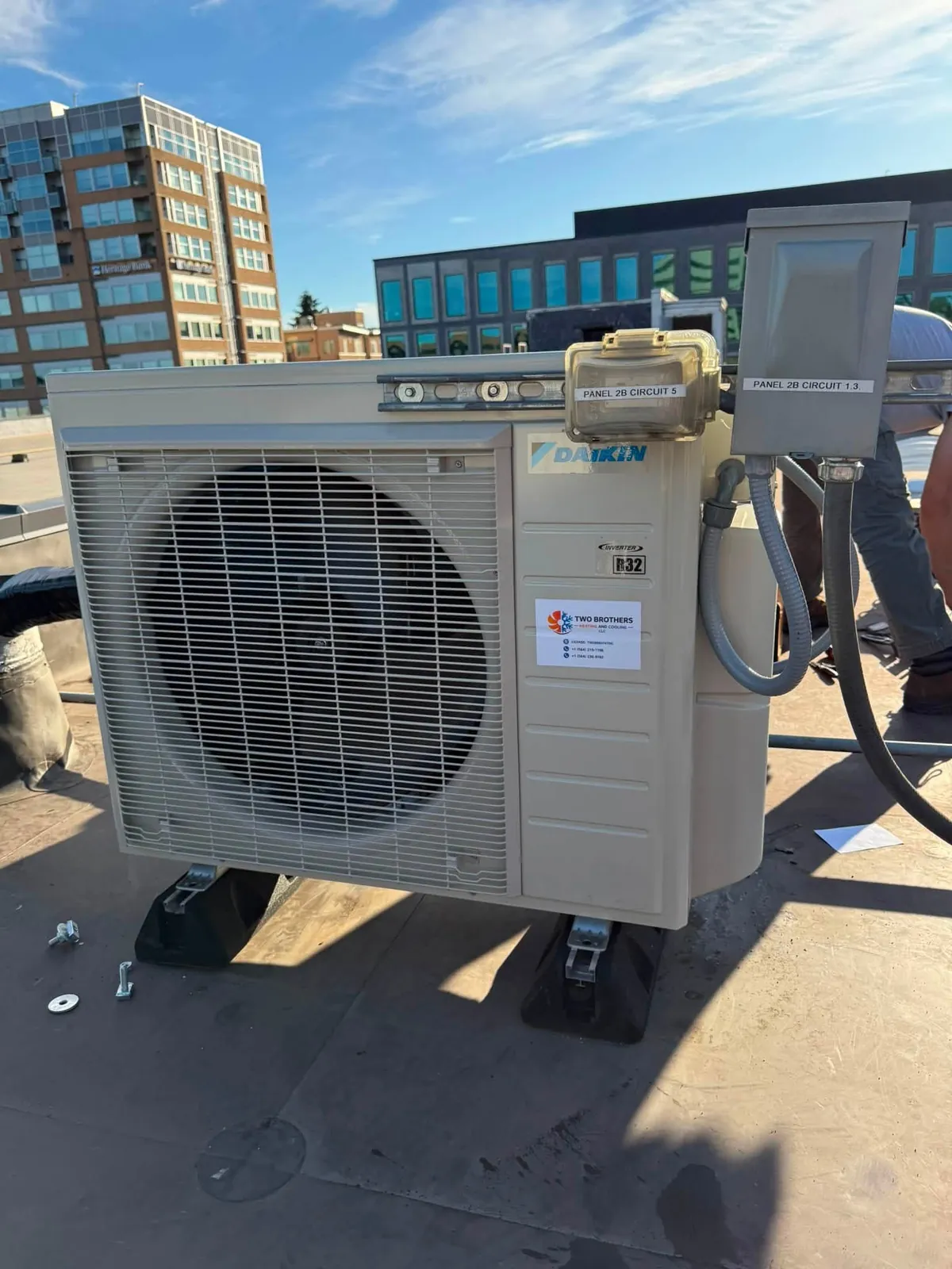 Cream ductless outdoor unit on a flat roof beside a glass office building